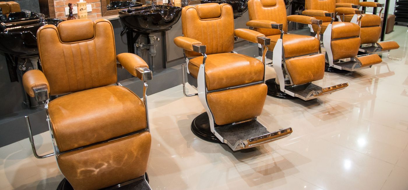 A row of tan leather barber chairs on a polished floor