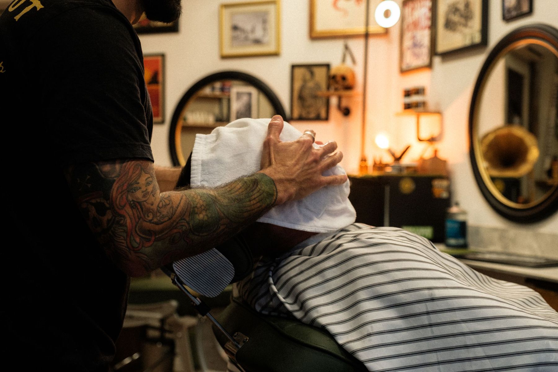 A barber pressing a hot towel over a reclined client’s face