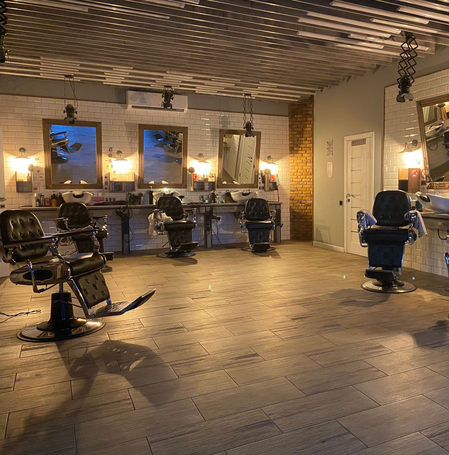 The shop floor after hours: black barber chairs, round mirrors and warm wall lamps over tiled floor