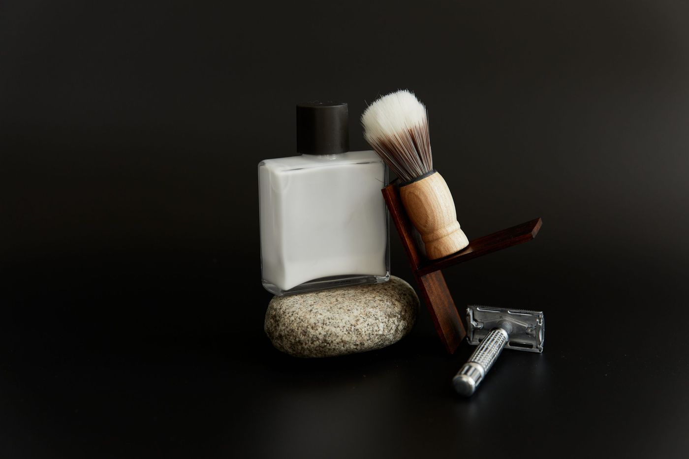 A shaving brush, a razor and a bottle of aftershave on a stone