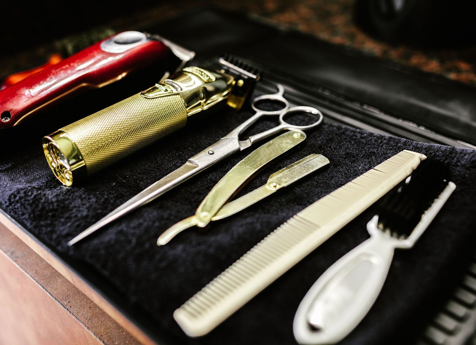 Clippers, a trimmer, scissors, a straight razor and combs laid out on a black towel