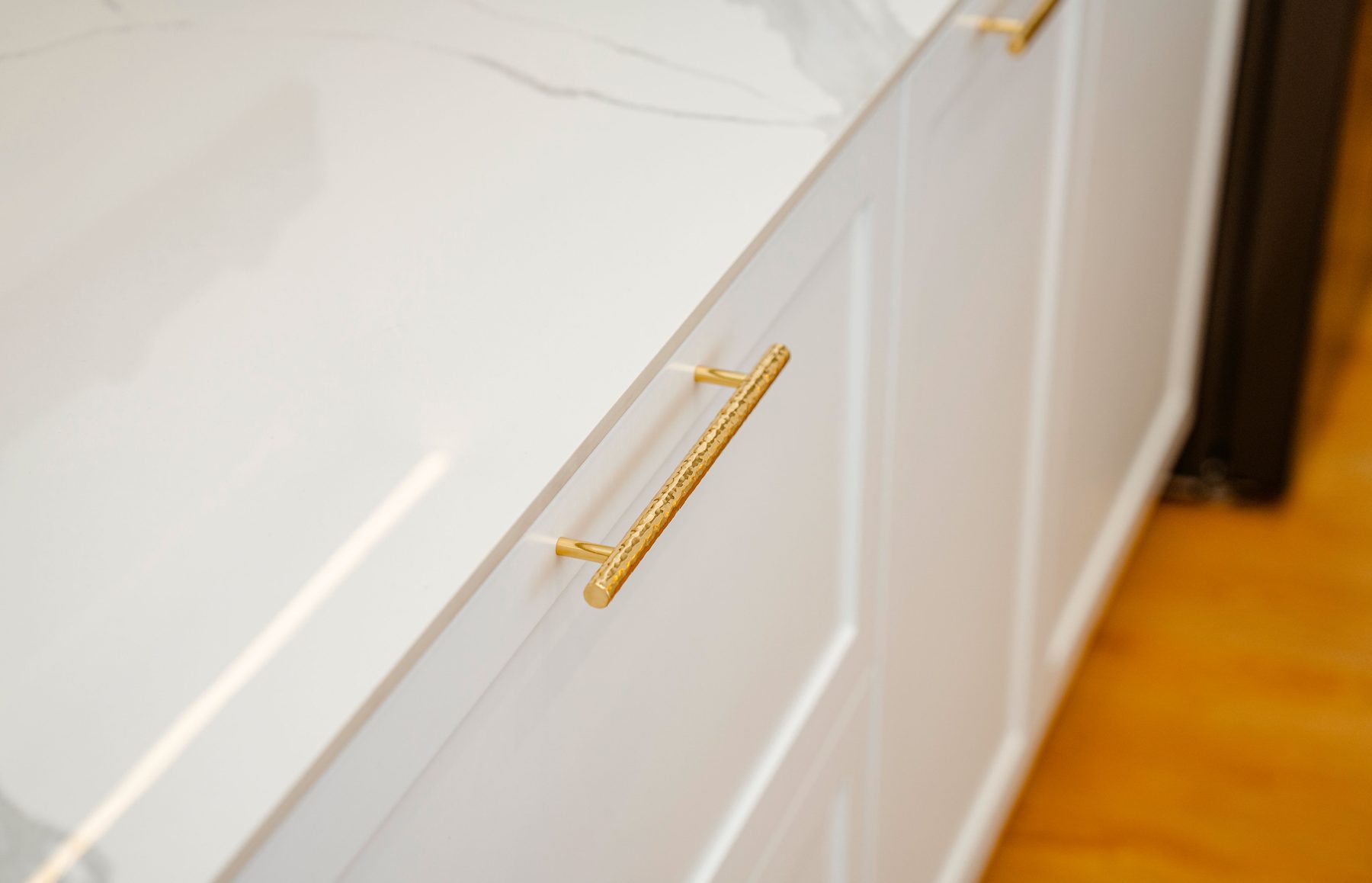 A brass bar pull on a white shaker cabinet under a marble-look counter