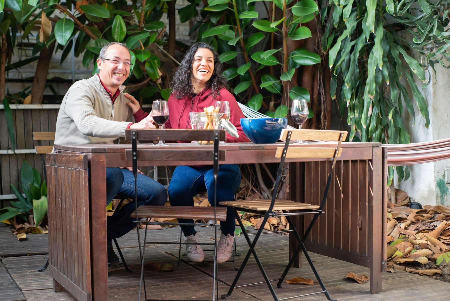 A couple laughing at a table on a wooden deck among tropical plants