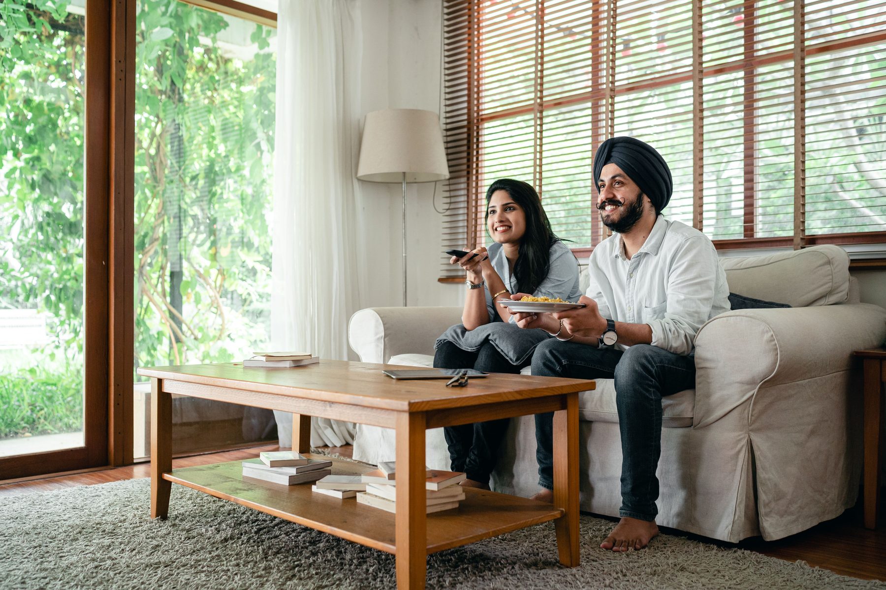 A couple on a sofa in a bright living room, one pointing a remote at the screen