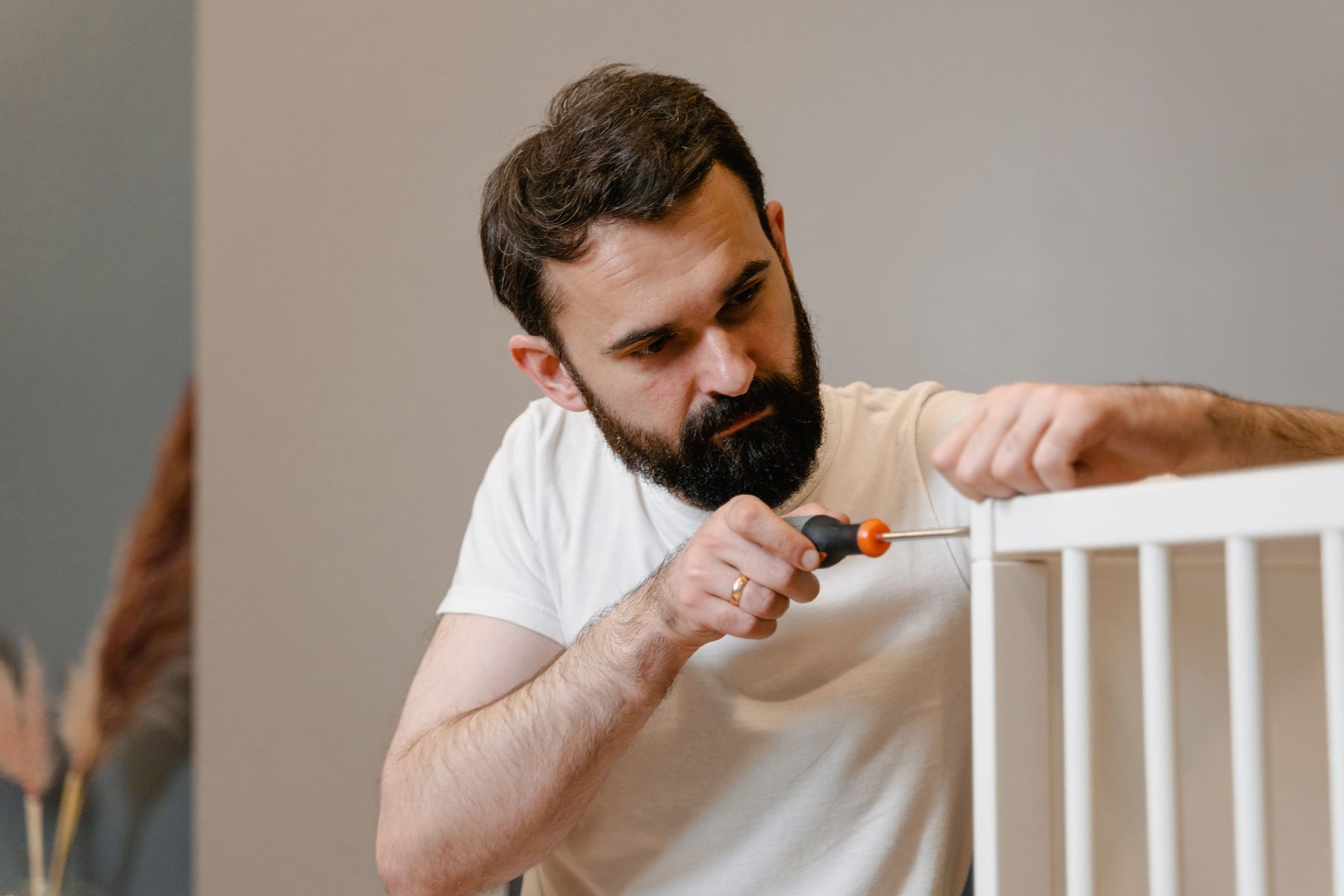 A man using a screwdriver on the top rail of a white crib