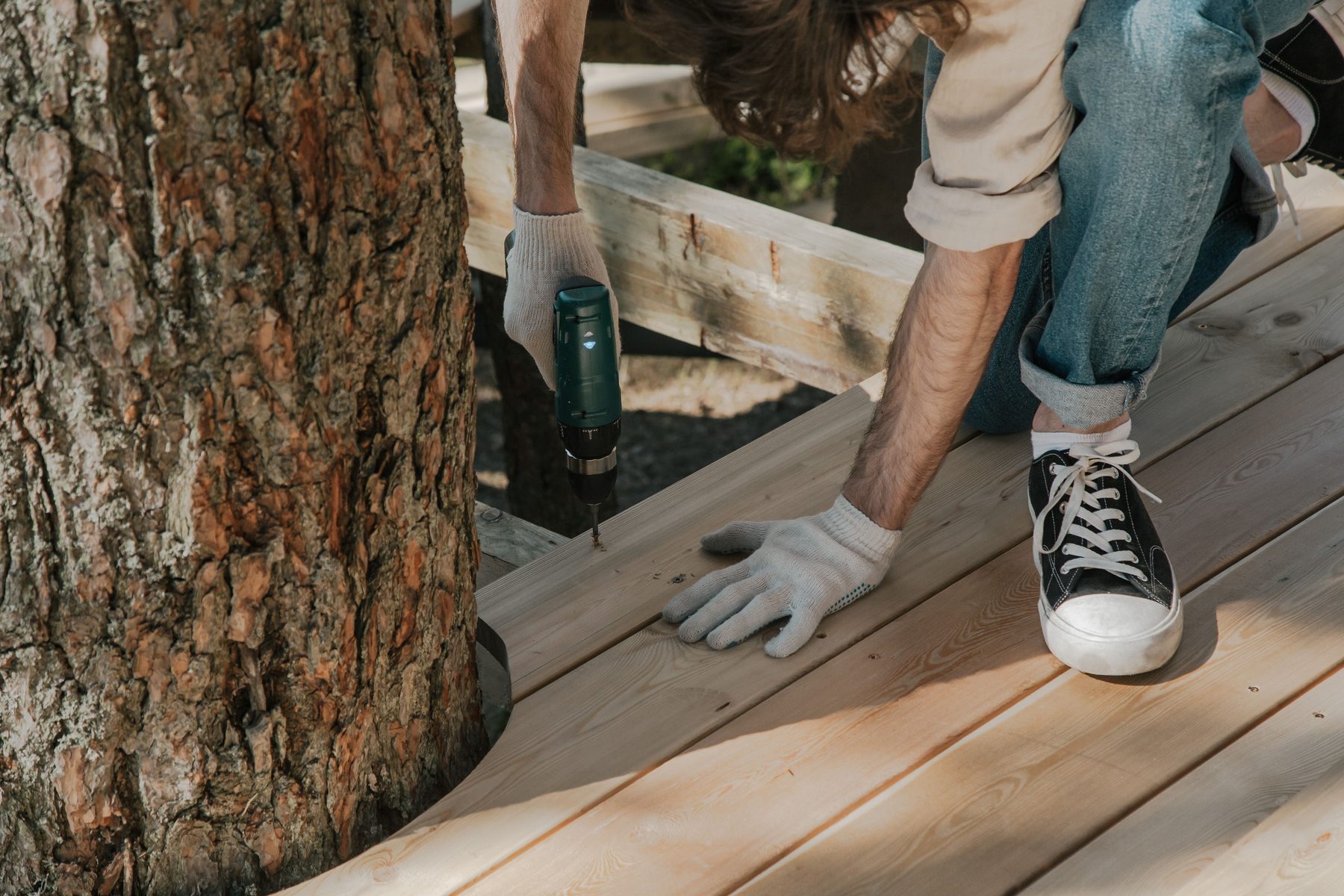 A man in work gloves screwing down new pale deck boards