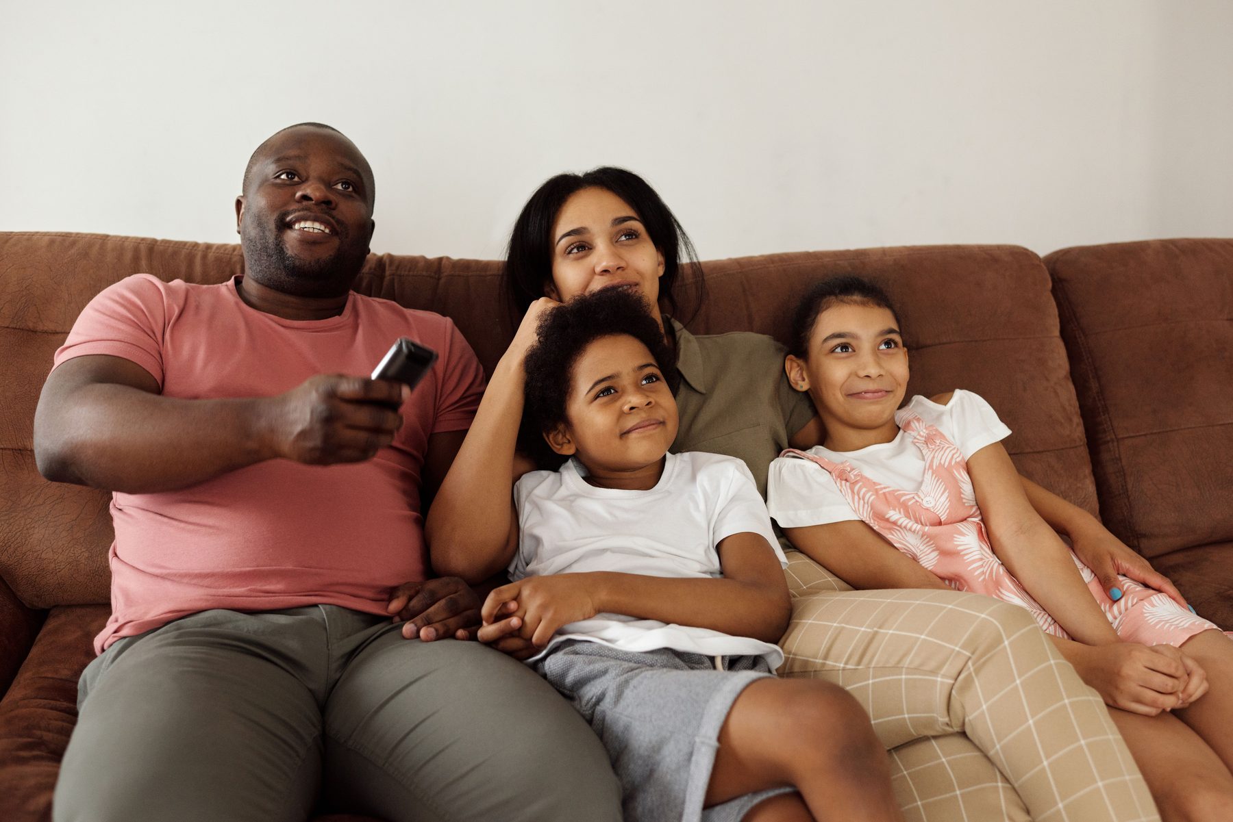 A family of four on a sofa, relaxed, looking at a screen off to one side