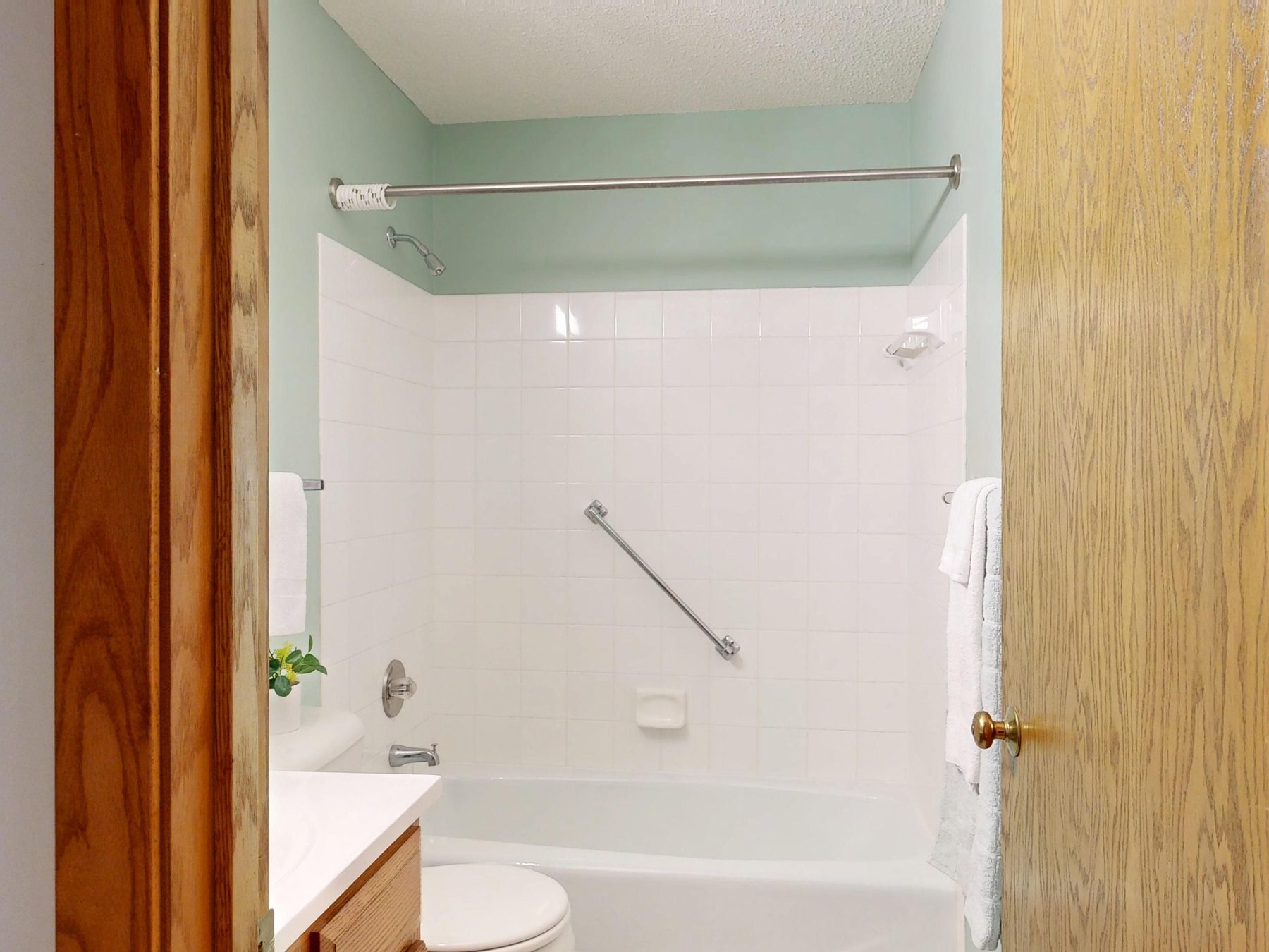 A white-tiled tub-shower surround with a stainless grab bar, the door ajar