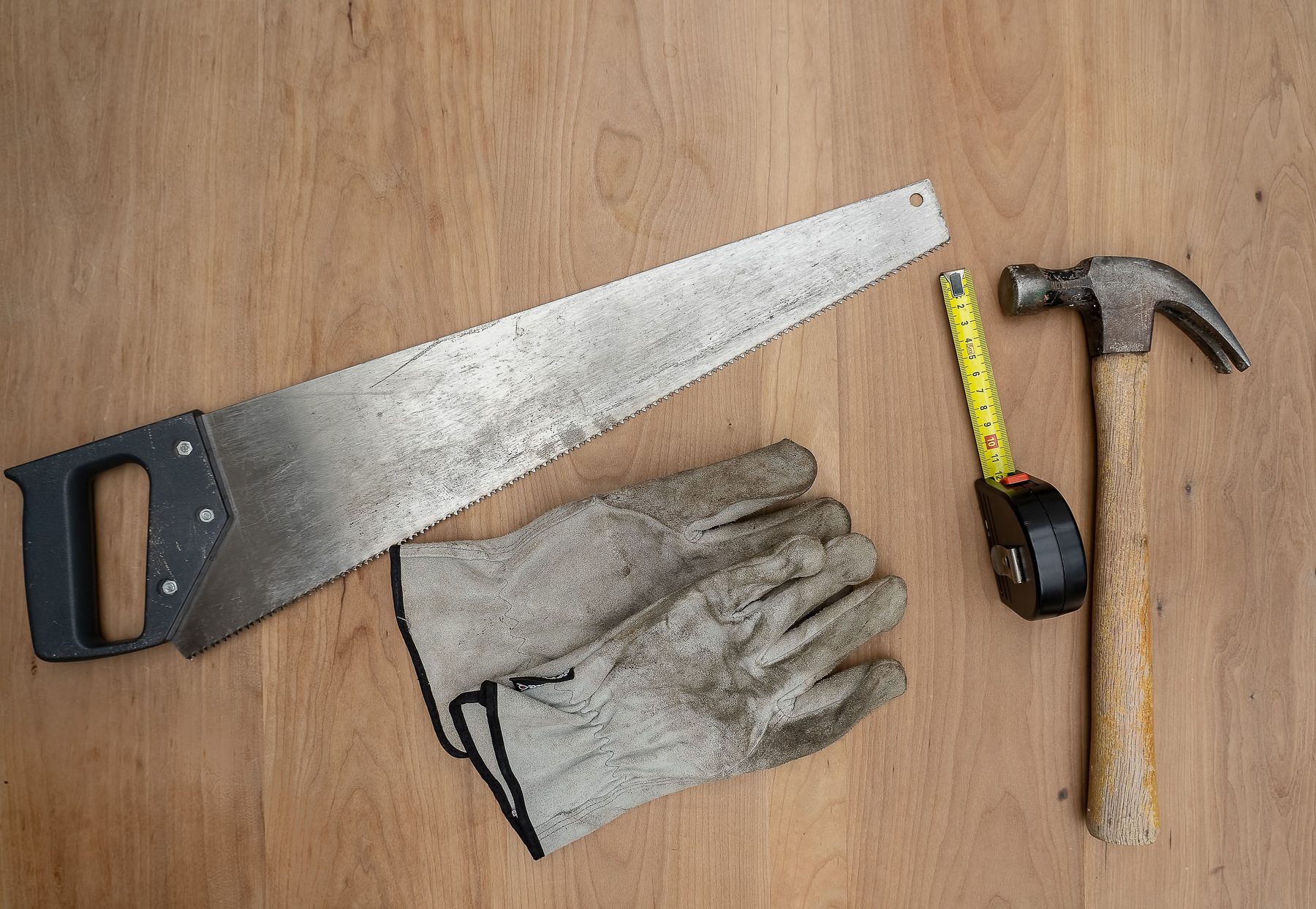 A handsaw, work gloves, a tape measure and a claw hammer on a wooden table