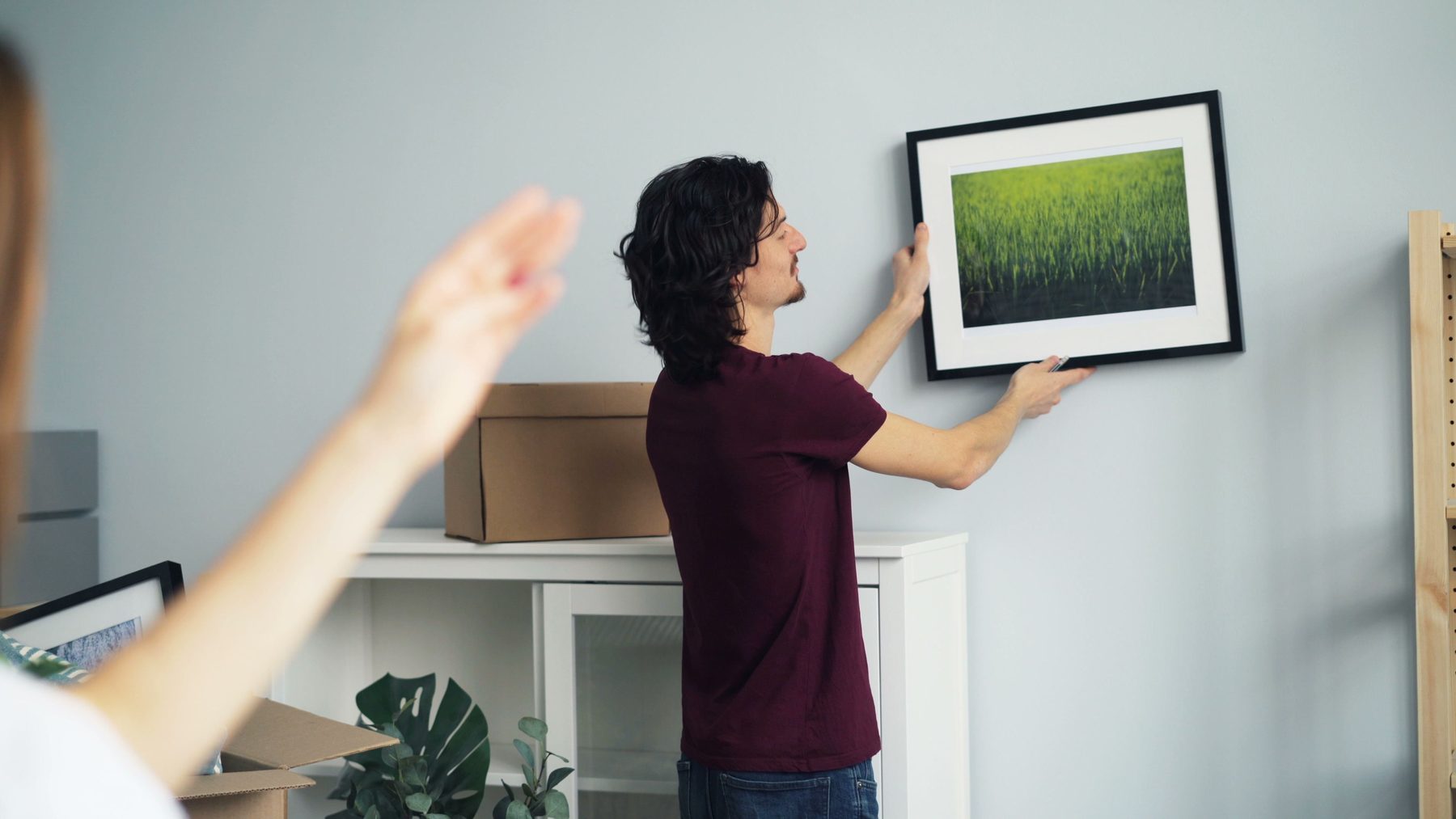 A man hanging a framed picture while a woman points out where it should go