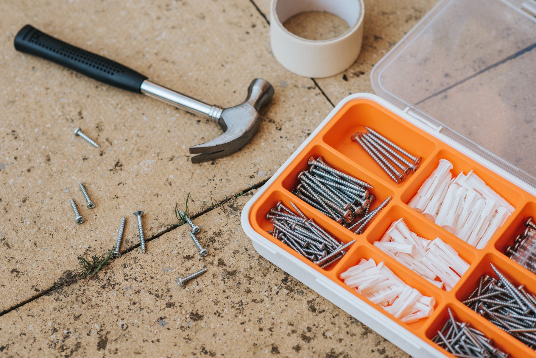 A claw hammer, masking tape and an organiser of screws and wall anchors