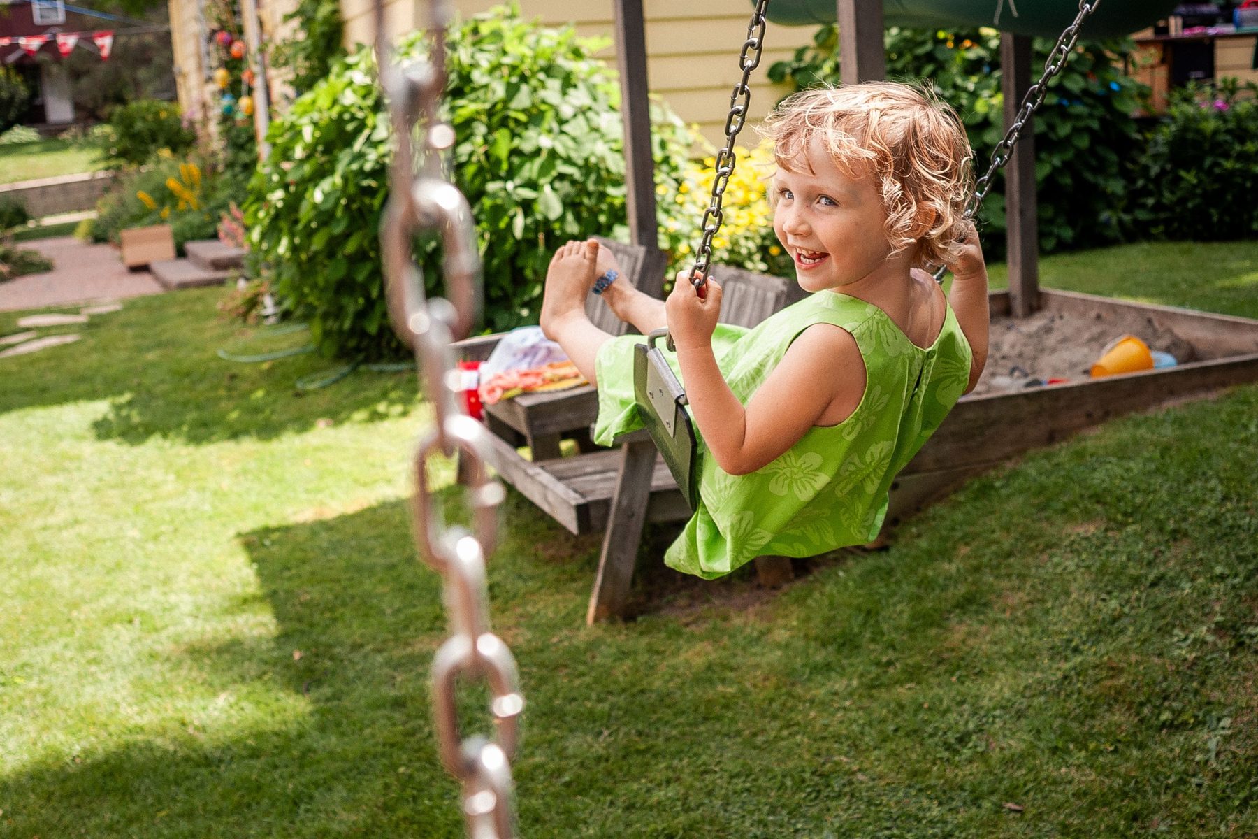 A little girl laughing on a swing in a sunny back yard