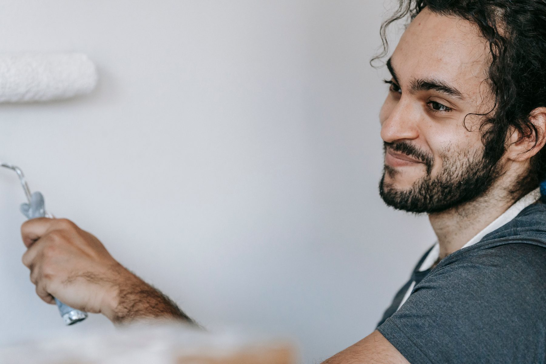 A smiling man in an apron rolling white paint onto a wall