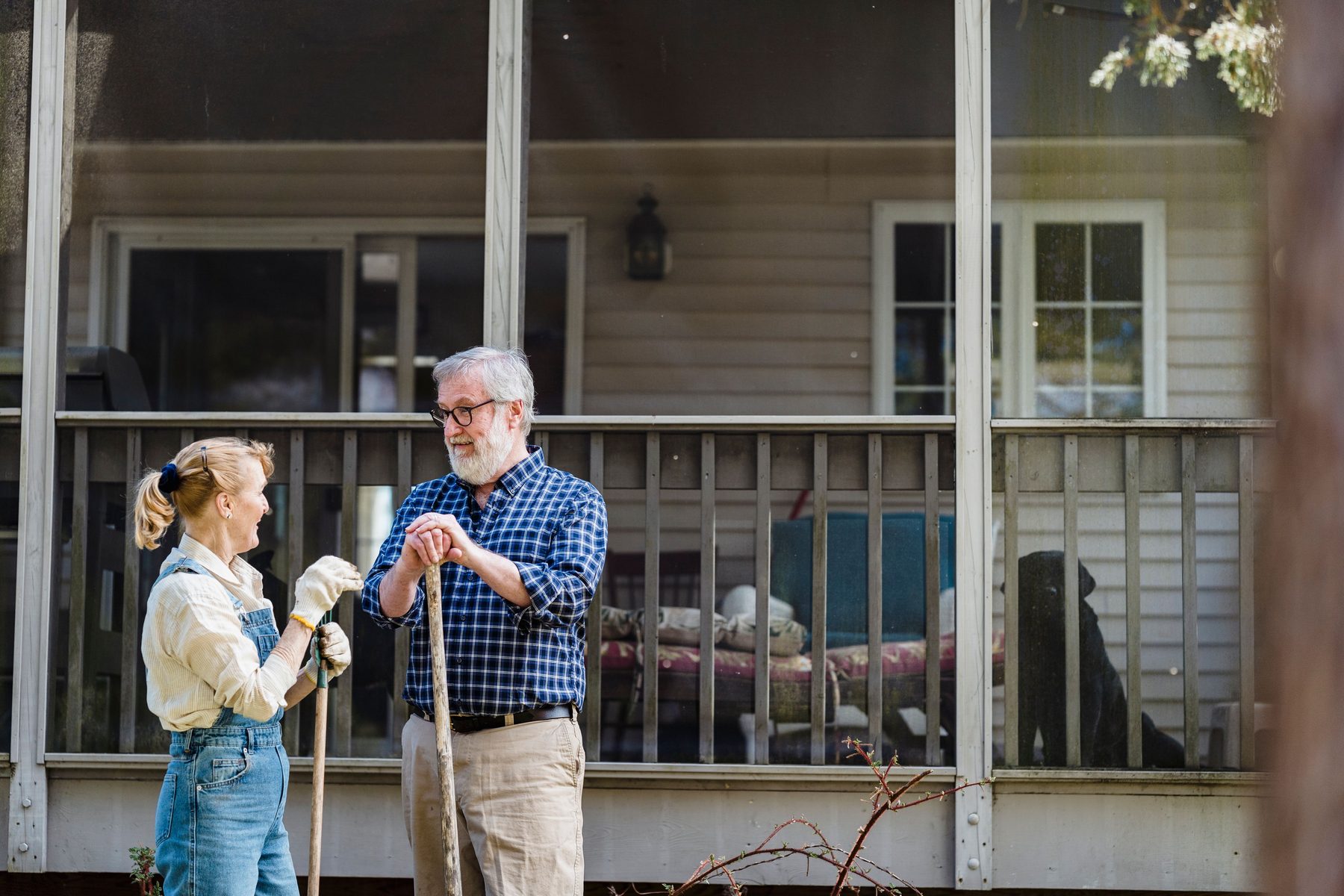 An older couple chatting outside a screened porch, garden tools in hand