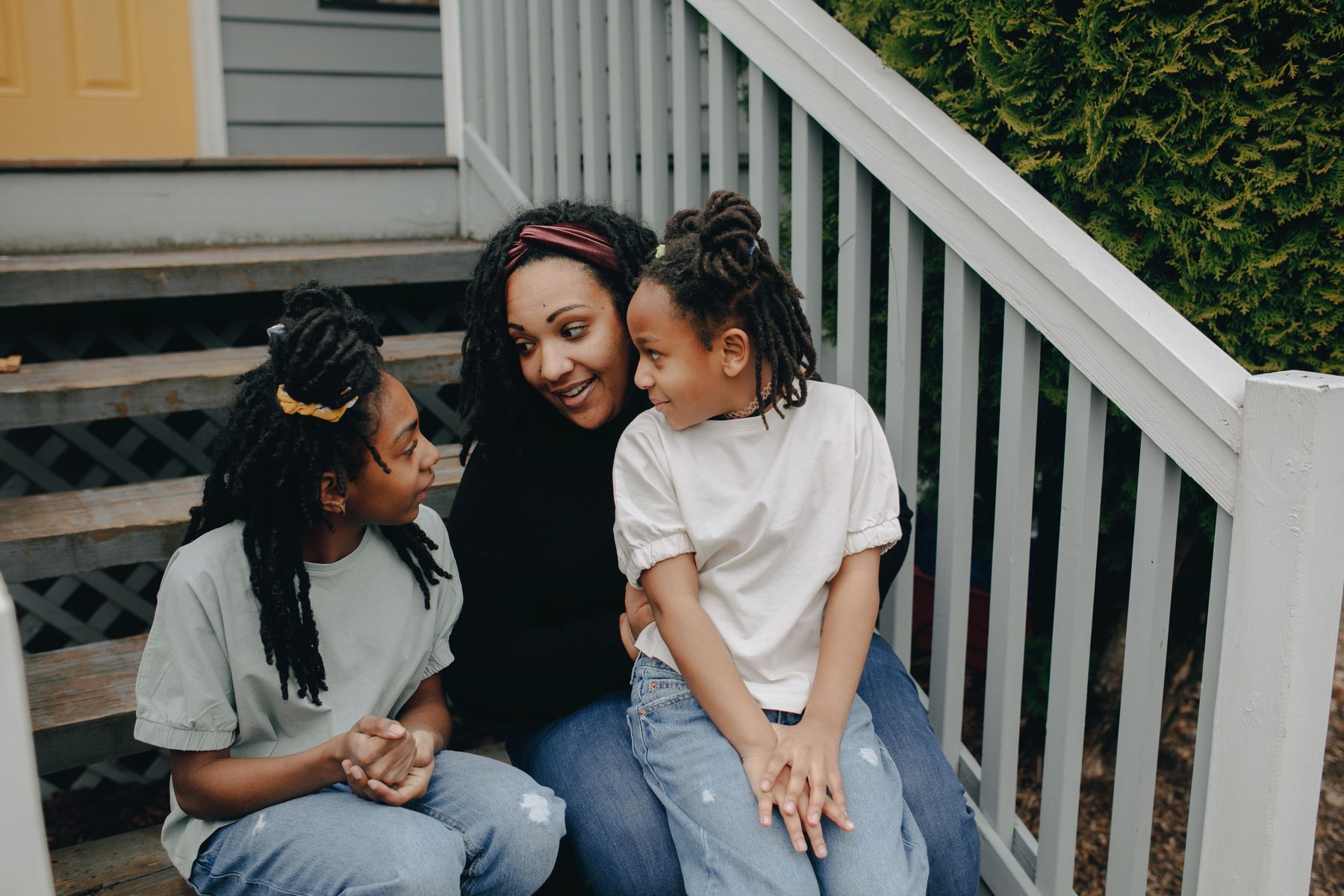 A mother and two daughters sitting together on painted porch steps