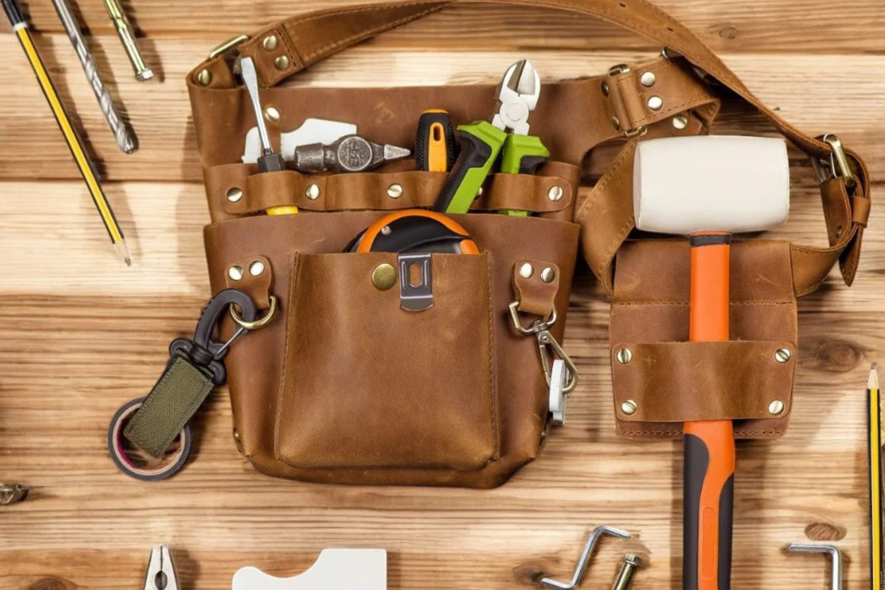 A leather tool belt with screwdrivers, cutters, a tape measure and a mallet, laid out on pine boards