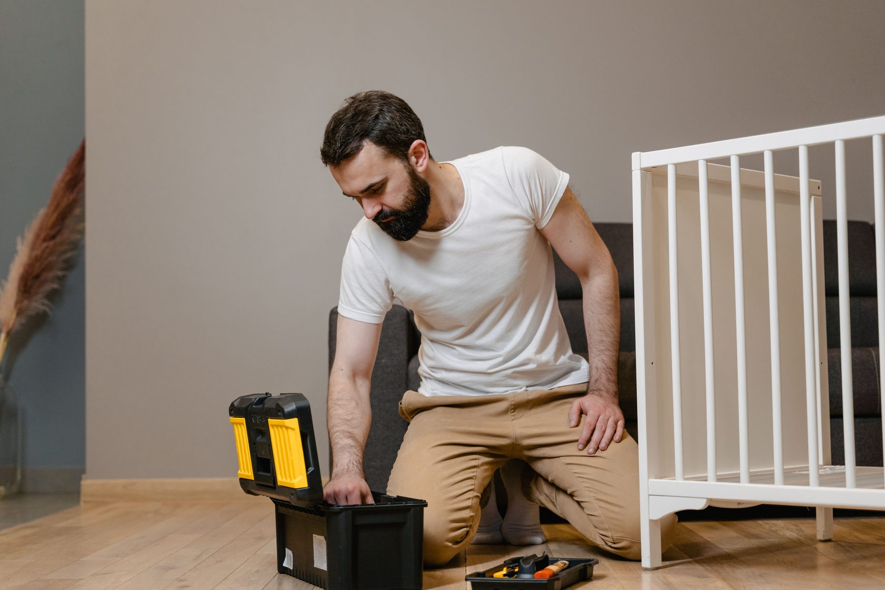 A man kneeling beside an open toolbox, a half-built white crib next to him