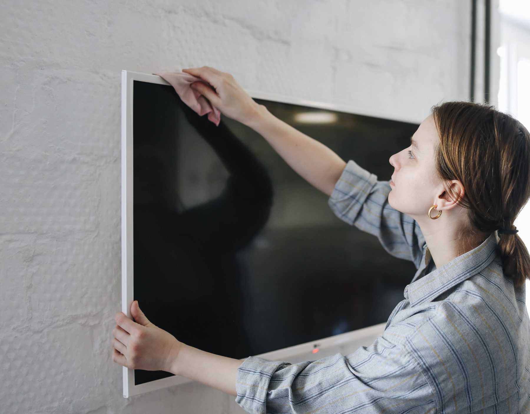 A woman straightening a flat-screen TV mounted on a pale wall