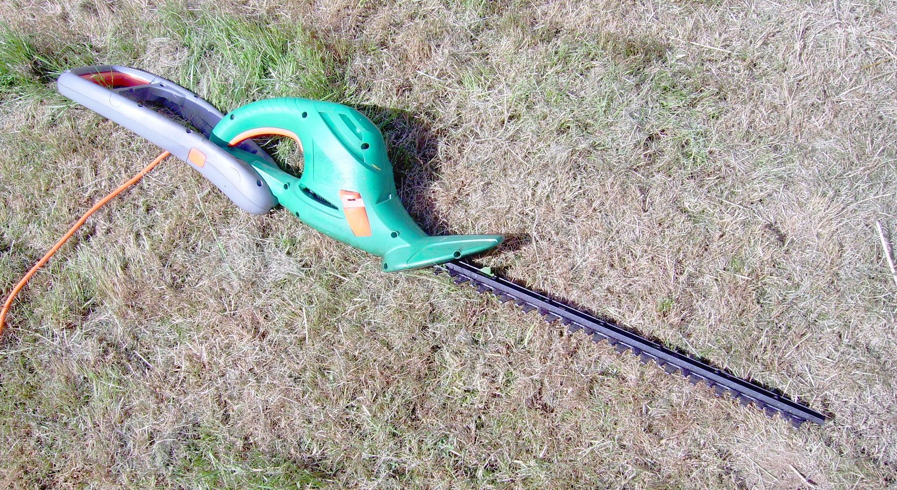 A powered hedge trimmer working along the top of a hedge