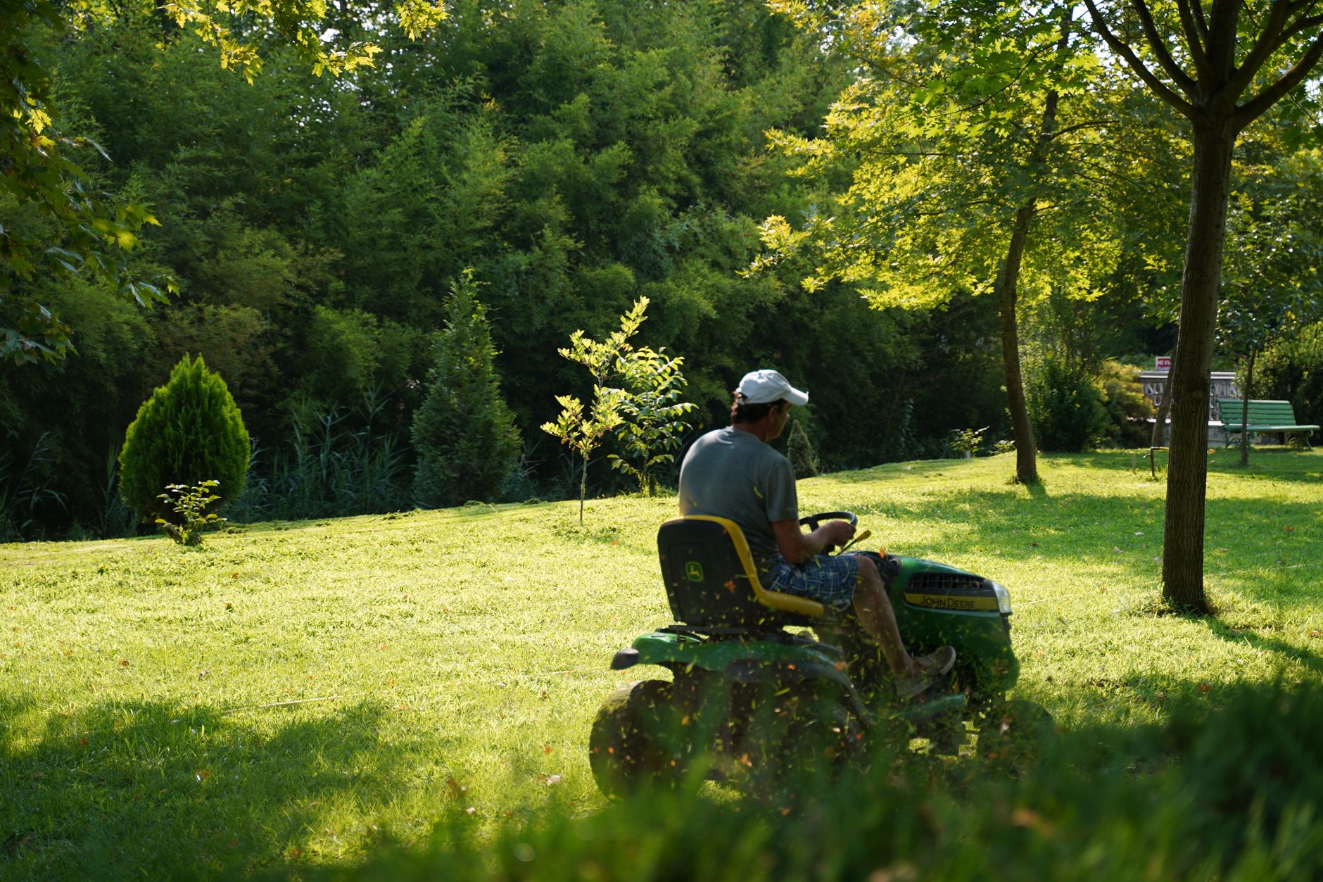 A crew member cutting a lawn on a ride-on mower, late afternoon