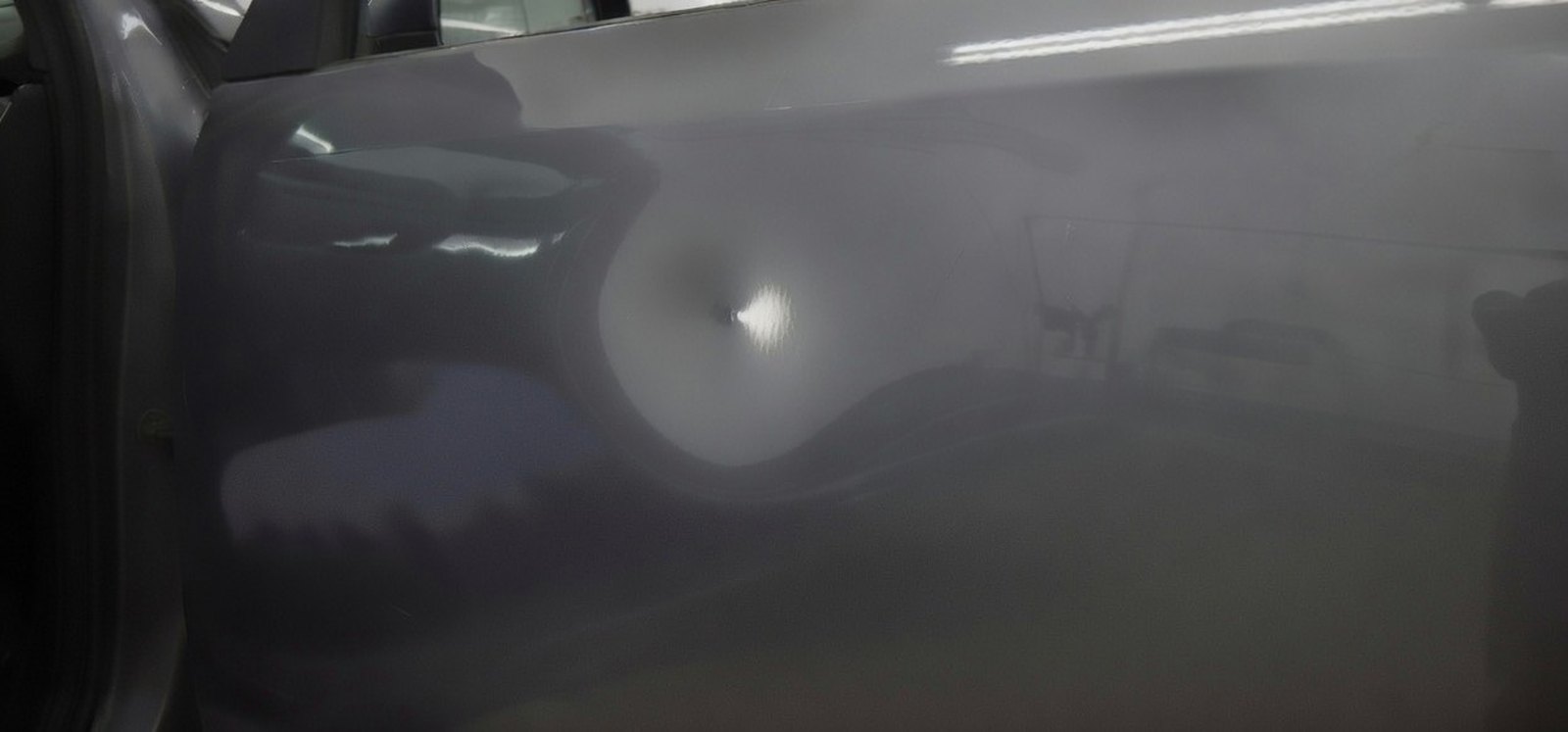 A shallow door ding in a dark grey car door panel, the paint unbroken