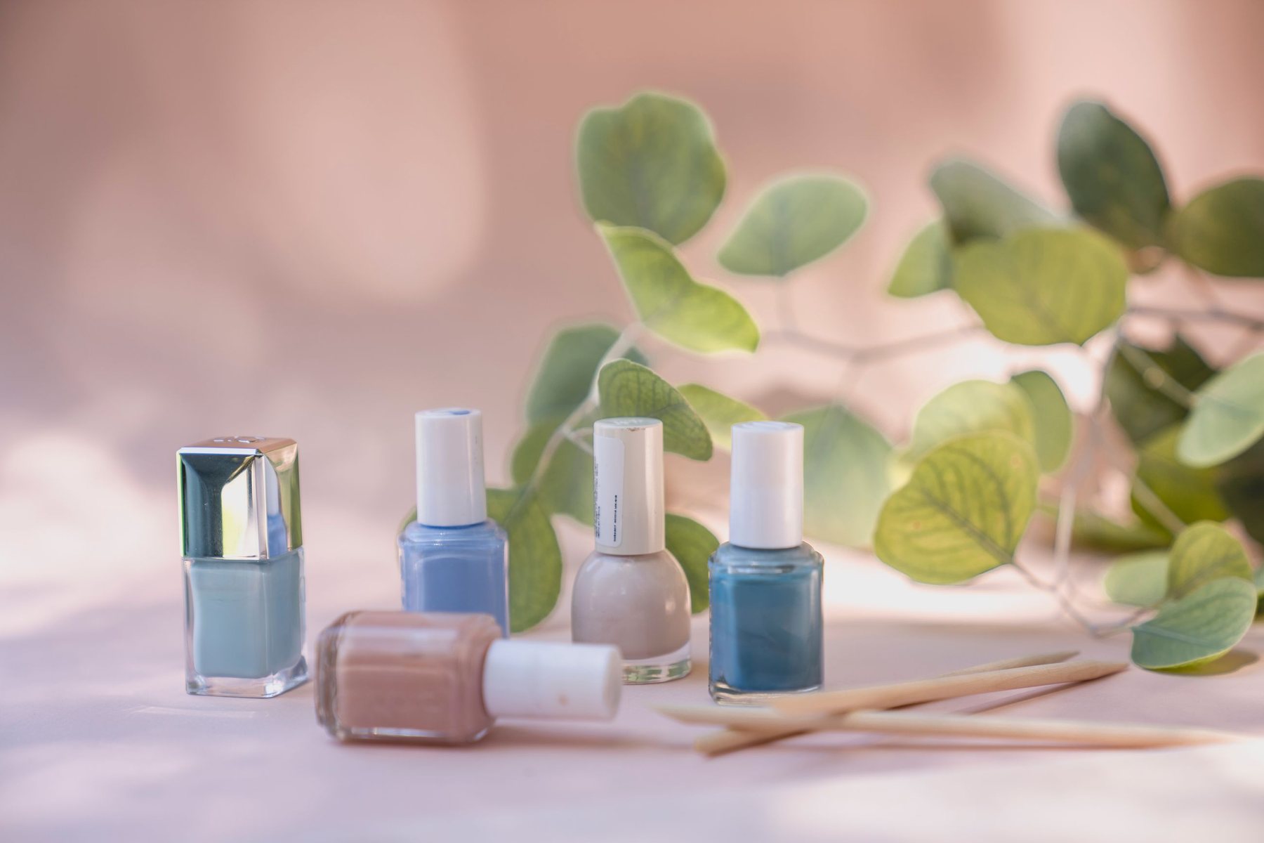 Pastel blue, nude and teal nail polish bottles with orange-wood sticks and eucalyptus