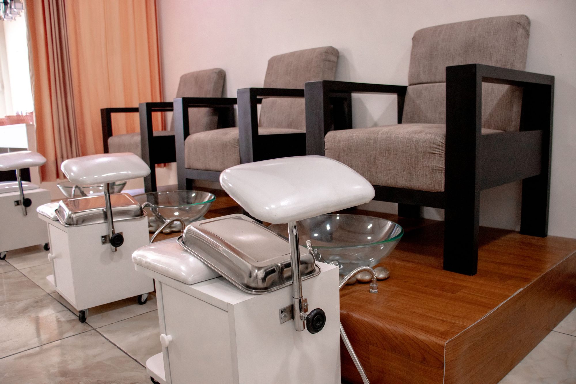 A row of pedicure chairs with glass basins and white footrests in a bright salon