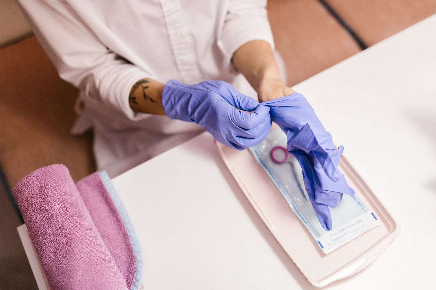 A technician in purple gloves opening a sealed pouch of sterilised tools on a pink tray