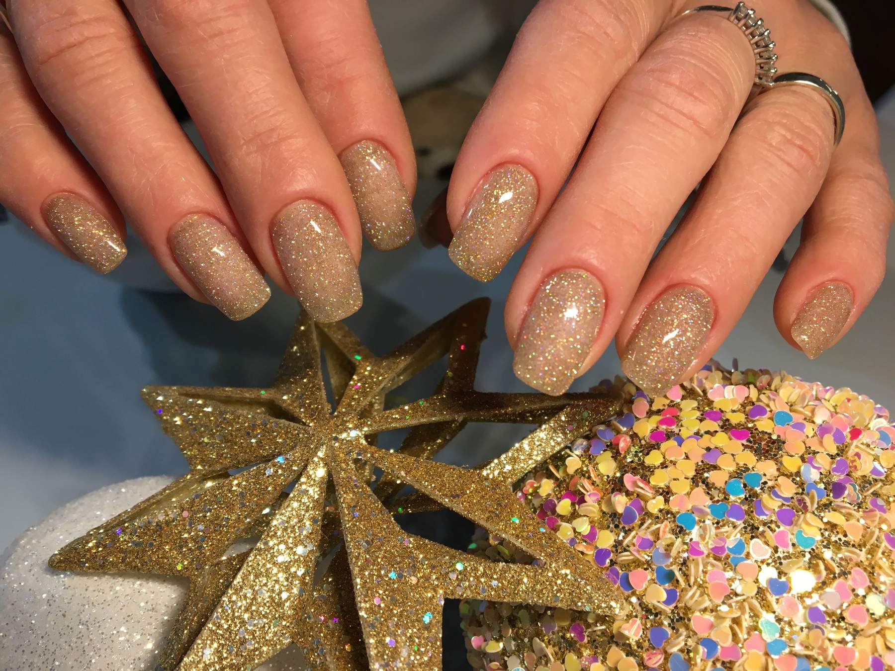 Square nails in a gold glitter finish beside a gold star ornament