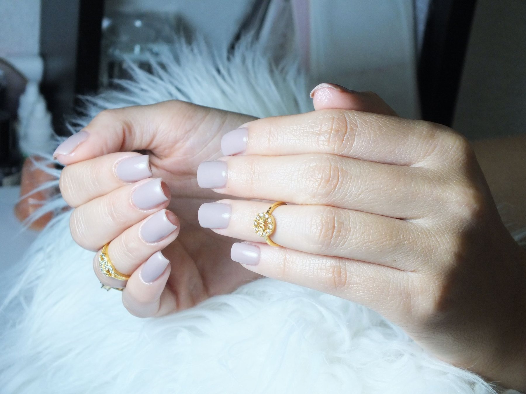 Short square nails in a soft lilac-grey finish on hands wearing gold rings
