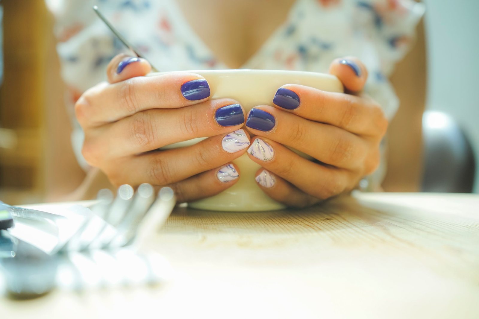 Periwinkle nails with two marble accent nails, hands around a cream bowl