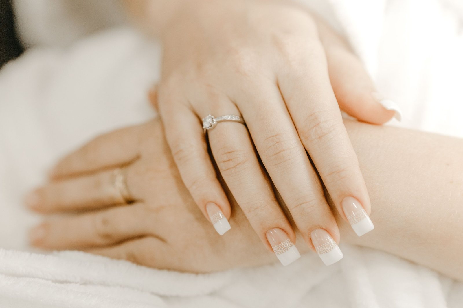 A classic French manicure with square white tips, a diamond ring on the hand