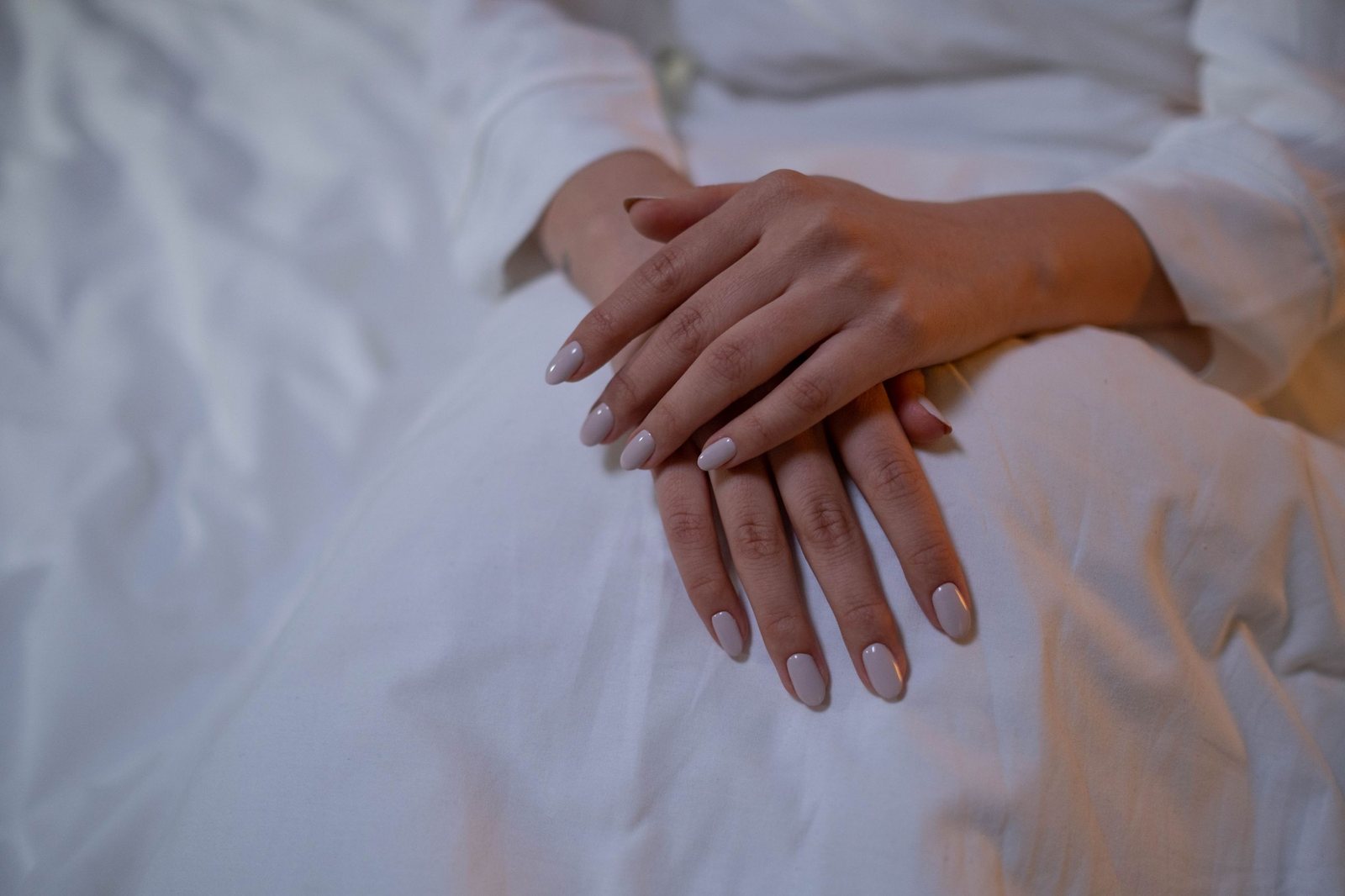 Hands with glossy nude almond nails resting on white linen