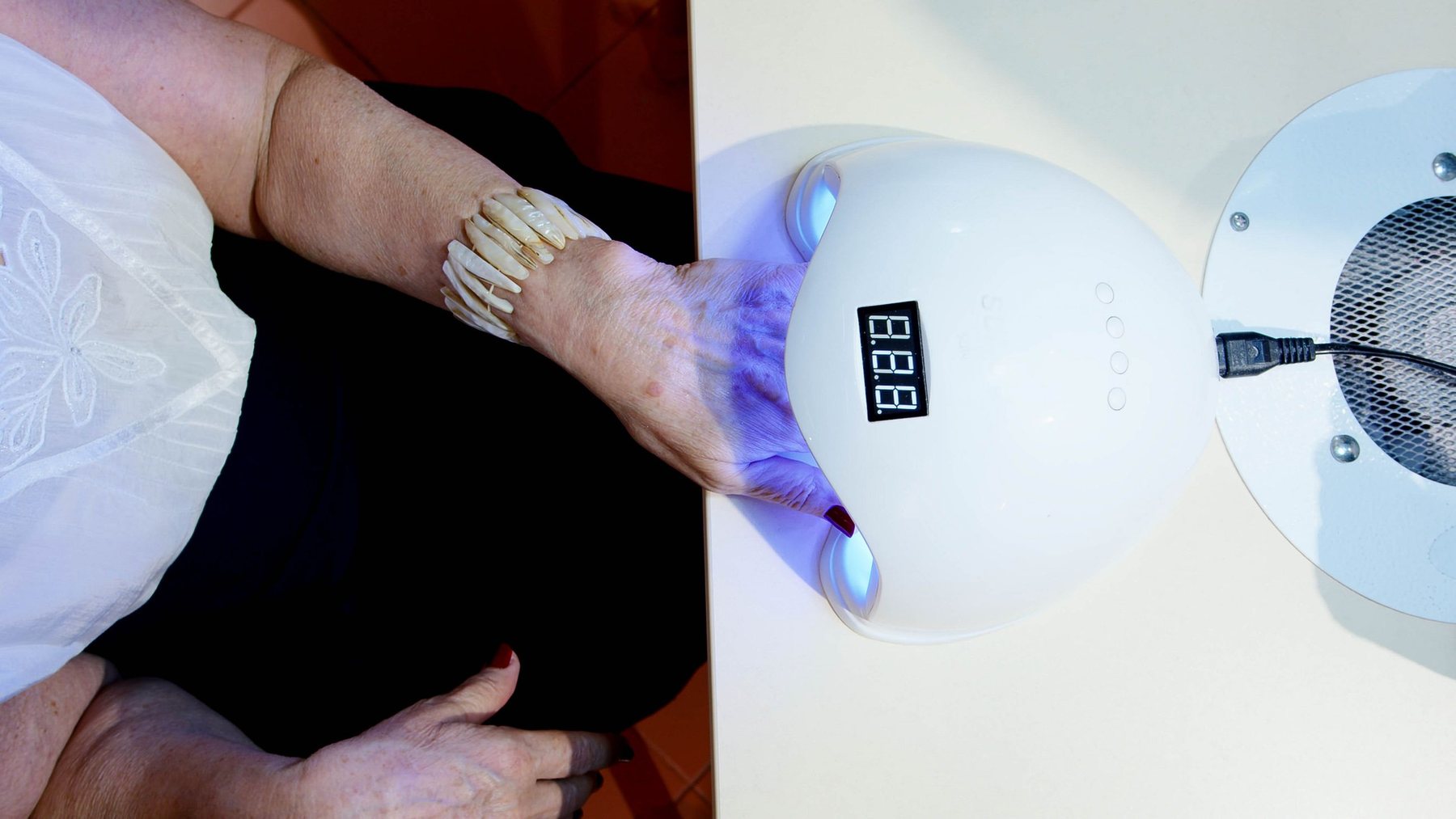A client's hand inside the LED lamp while the gel cures, the dust collector beside it