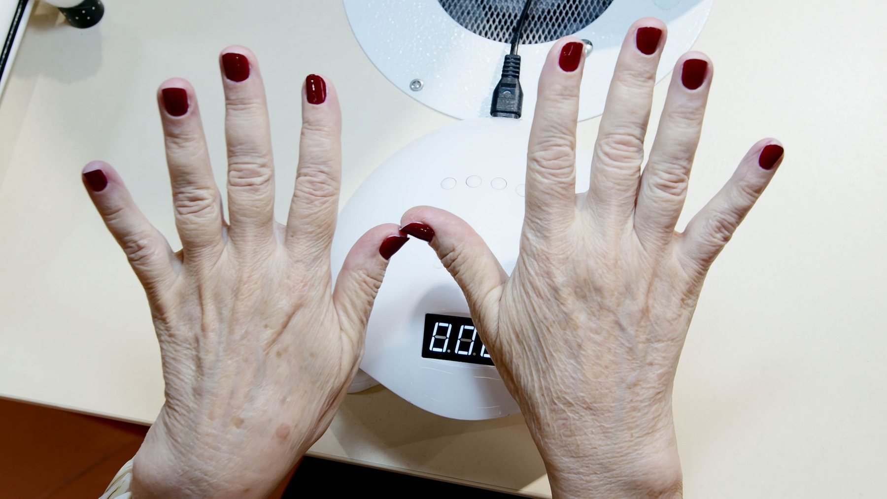 Two hands with fresh red gel polish spread over the white LED curing lamp