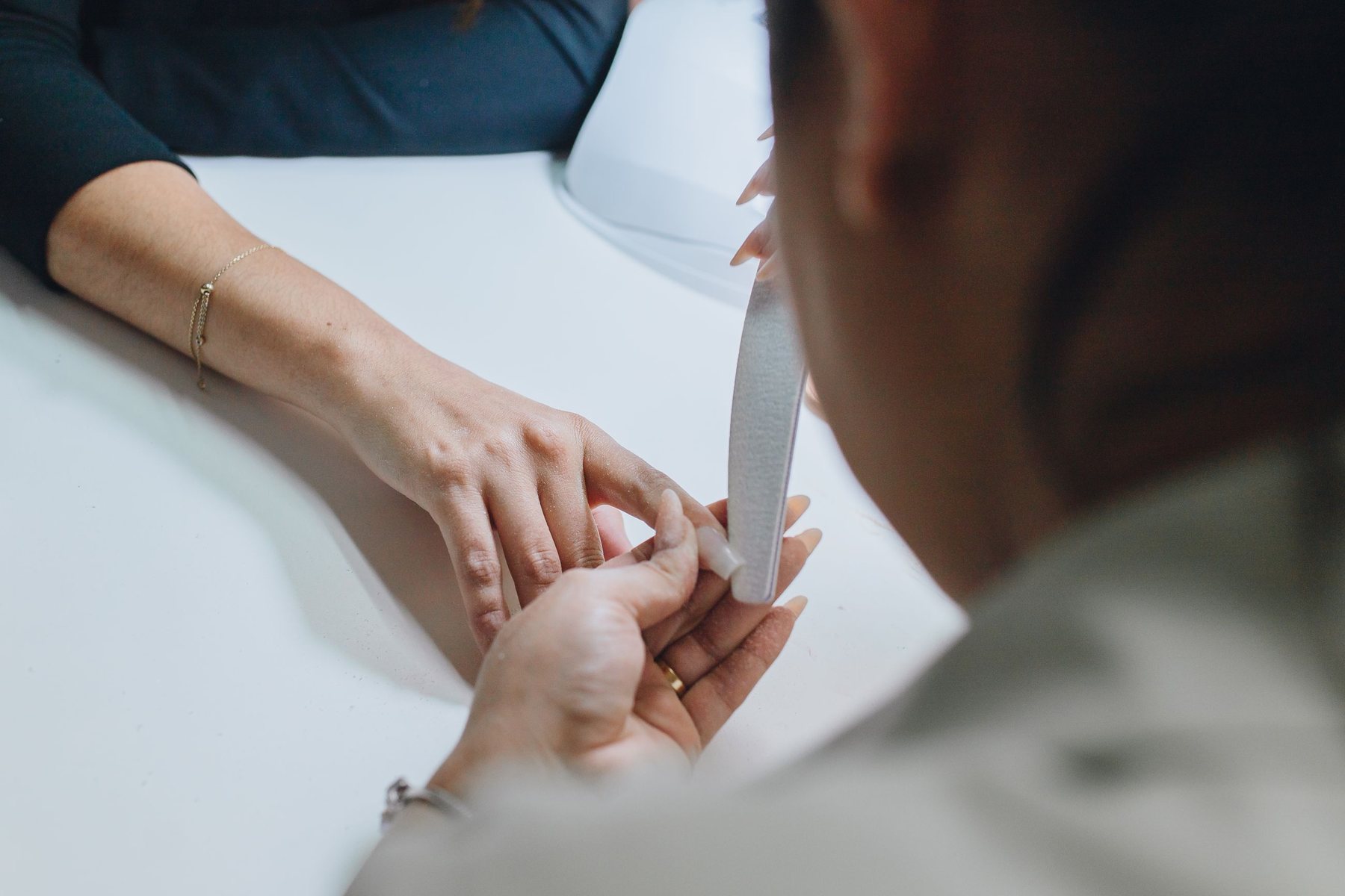 A manicurist shaping a client's nails with a file at a white table