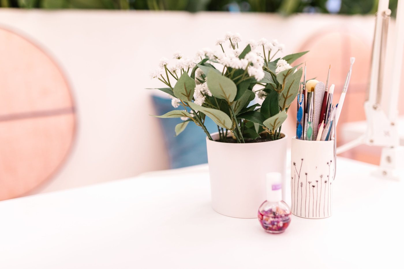 A white manicure table with a potted plant, a cup of brushes and a bottle of cuticle oil