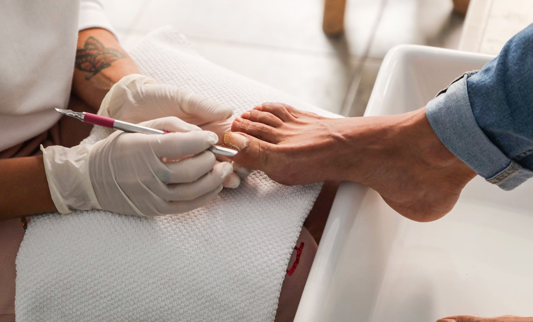 A gloved technician tidying the cuticles of a client's foot resting on a towel over the basin