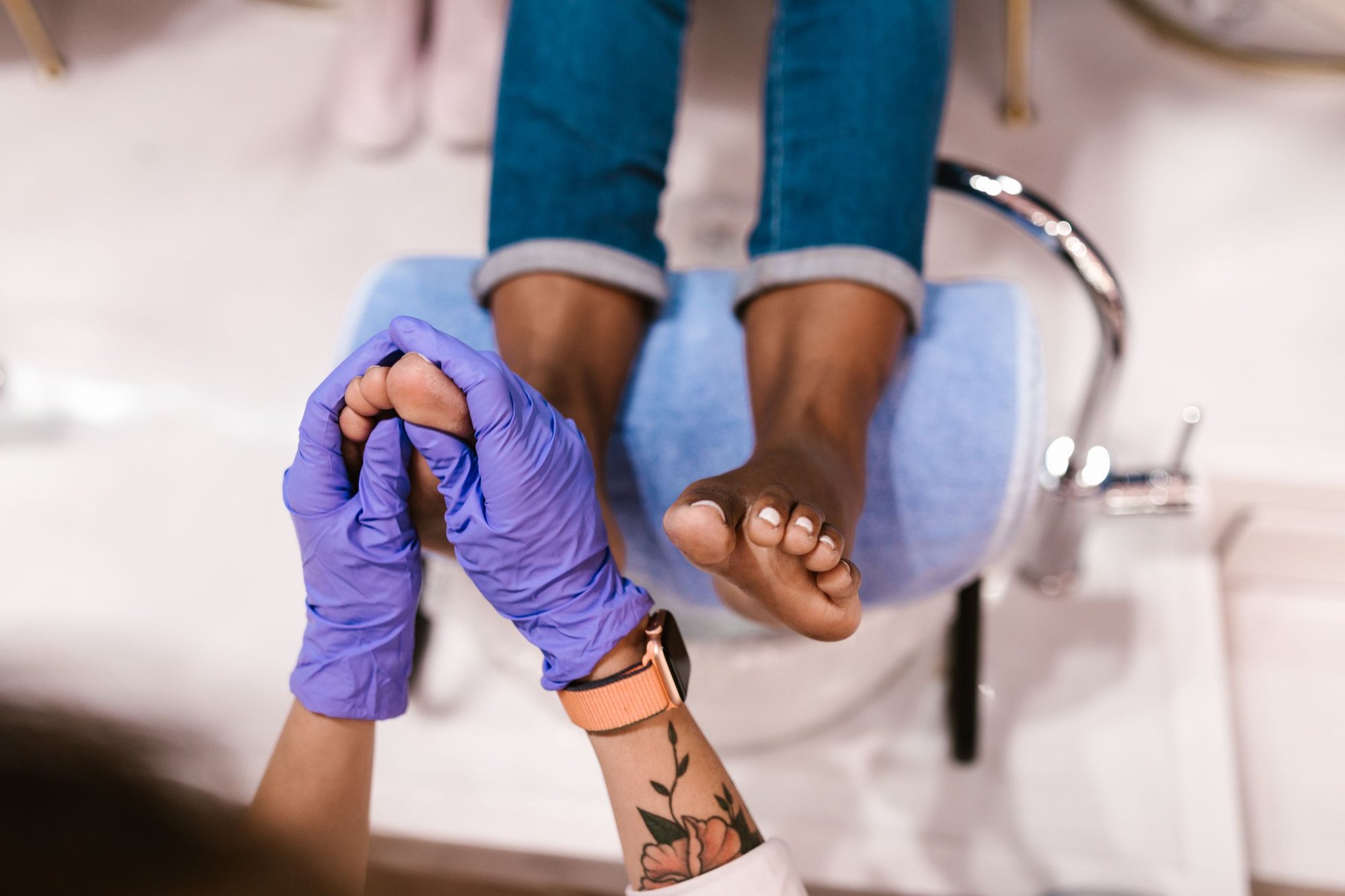 A client's feet on the rest of a pedicure chair while a technician in purple gloves works on the toes