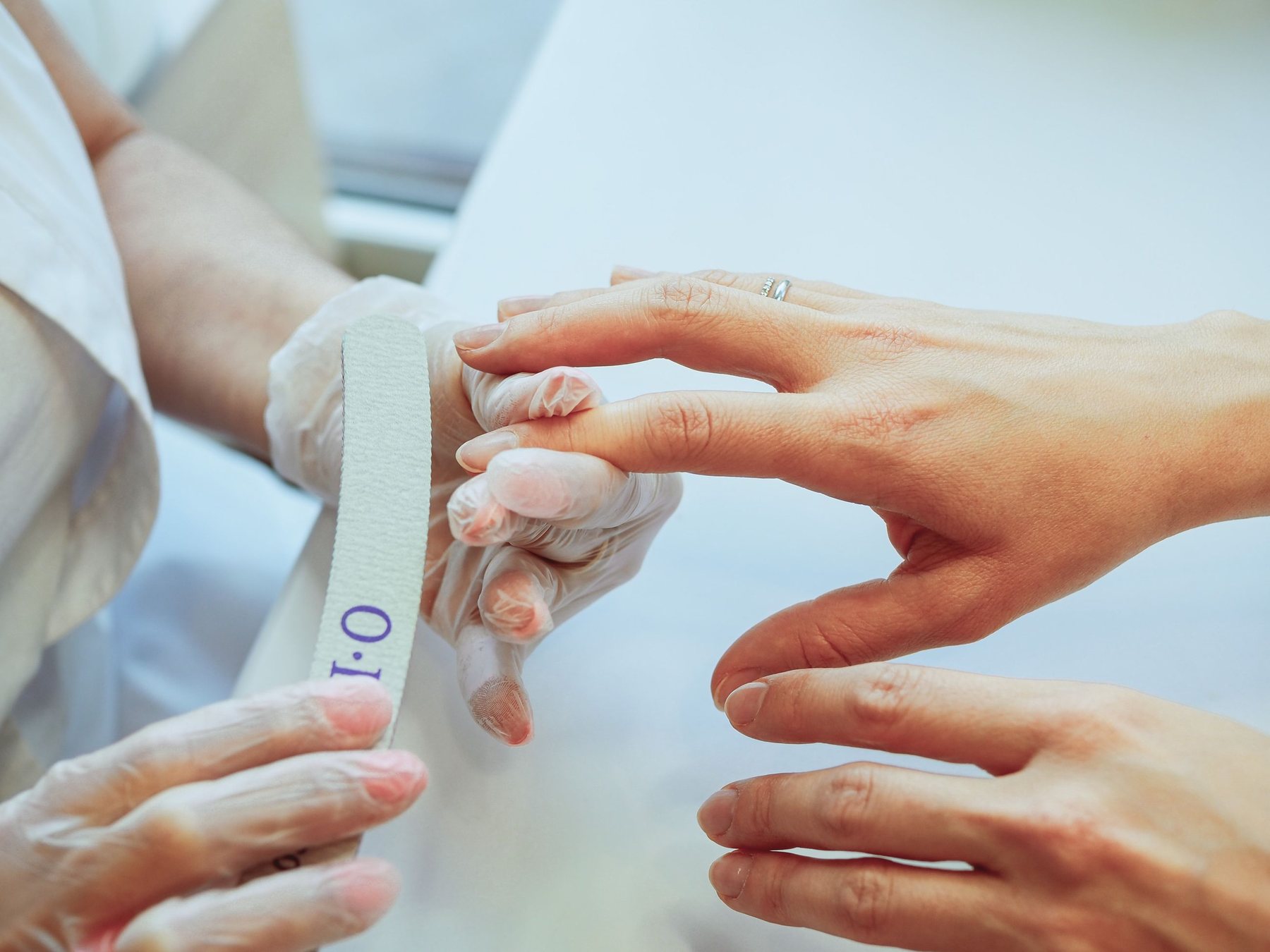 A technician in clear gloves shaping a client's nail with a file