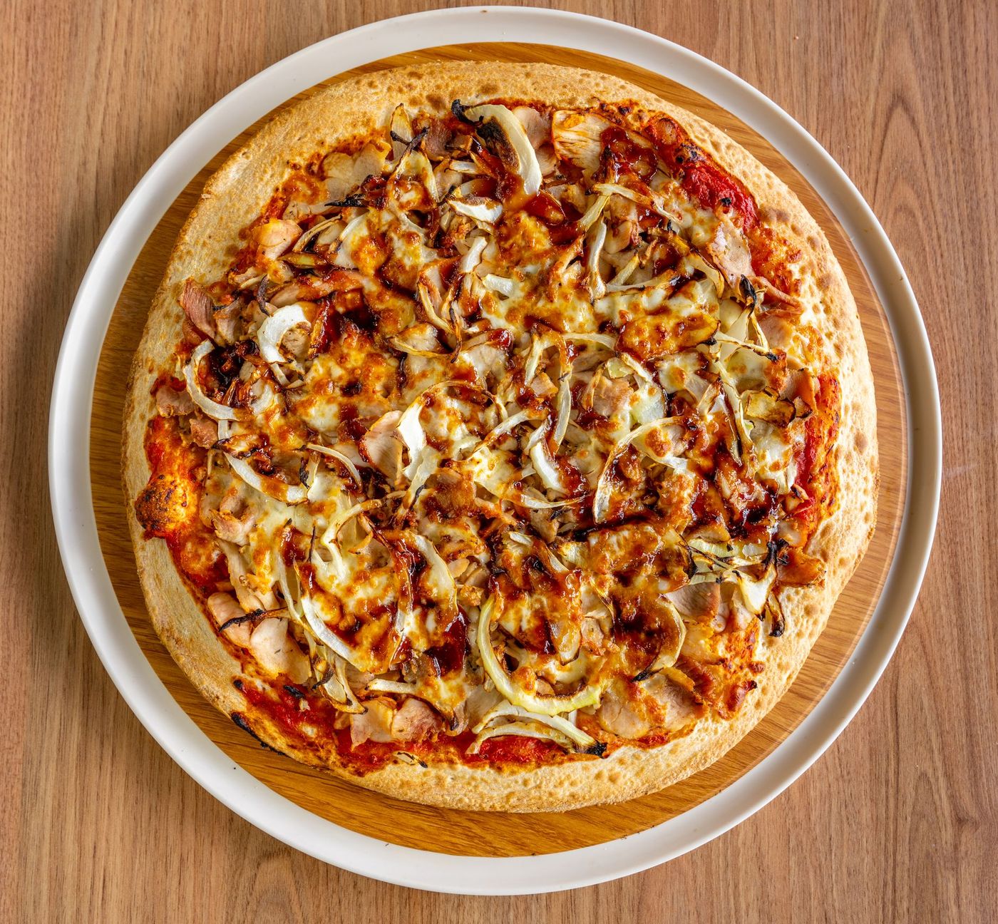 Overhead BBQ chicken pizza with sliced chicken, roasted onions, melted mozzarella and a barbecue sauce drizzle