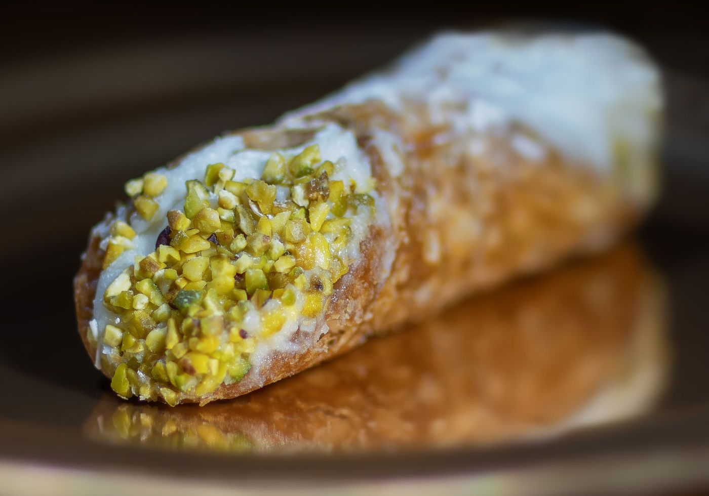 A Sicilian cannoli with crisp fried shell and ricotta filling, ends dipped in chopped pistachio