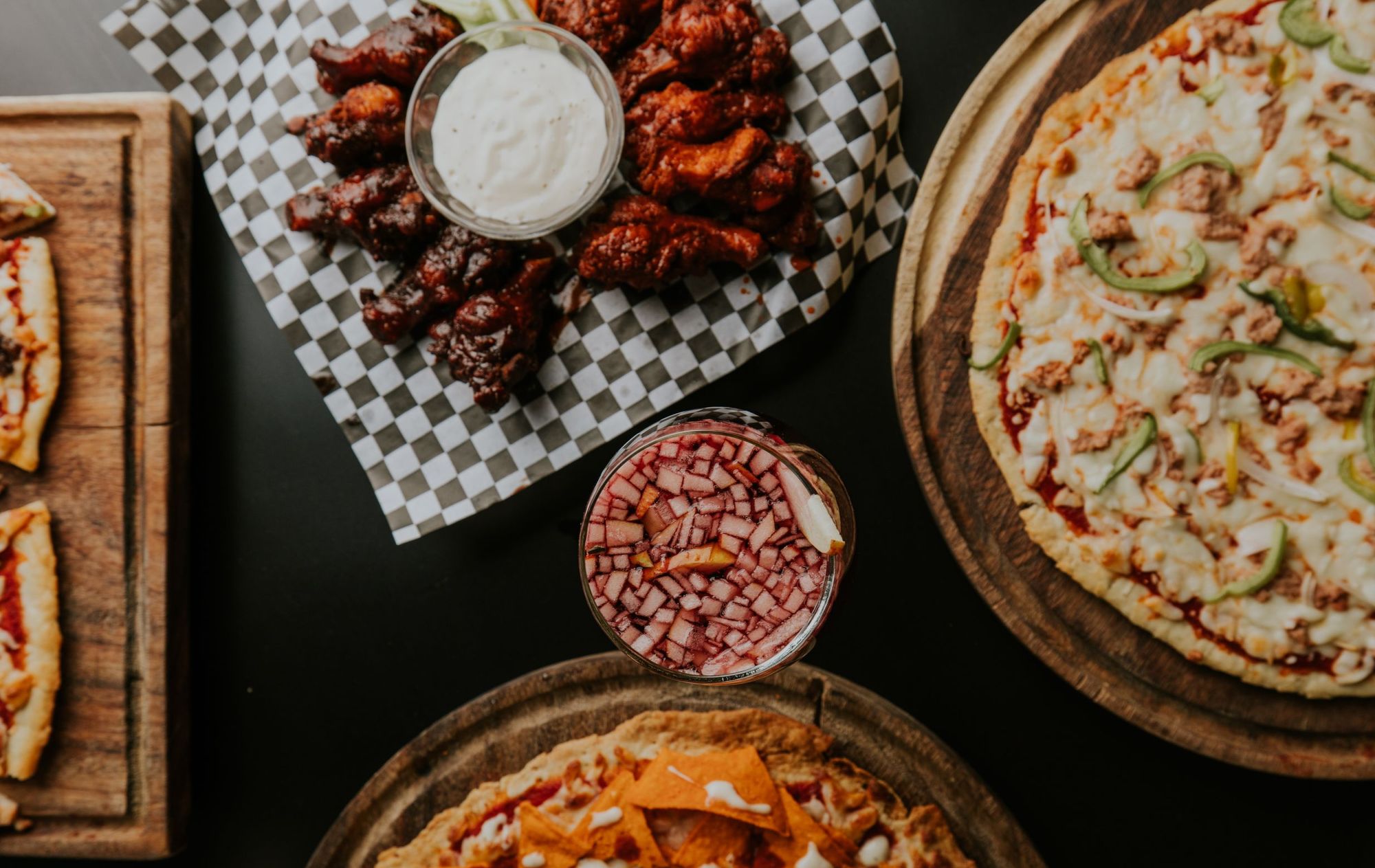 Catering spread from above: pizzas on boards, barbecue wings with ranch and pizza slices