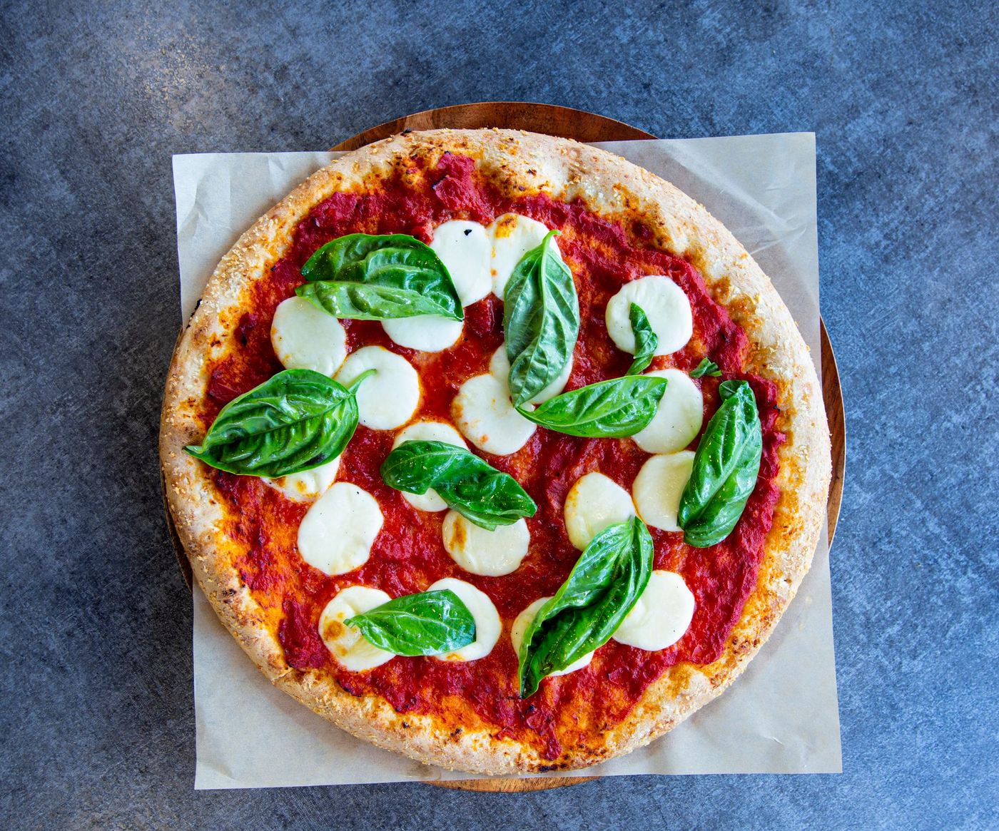 Overhead margherita pizza with tomato sauce, rounds of fresh mozzarella and whole basil leaves on parchment