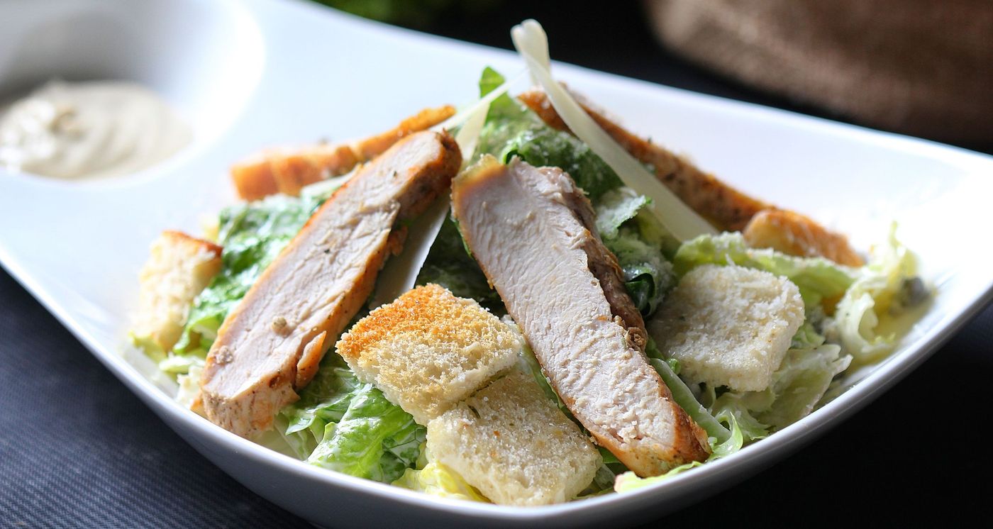 Chicken Caesar salad with romaine, sliced chicken, croutons and shaved parmesan in a white bowl