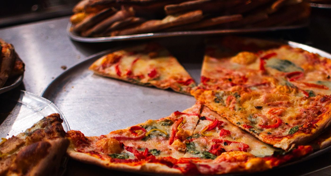 Thin-crust pizza with red peppers and spinach, cut into slices on a steel pan at a pizzeria counter