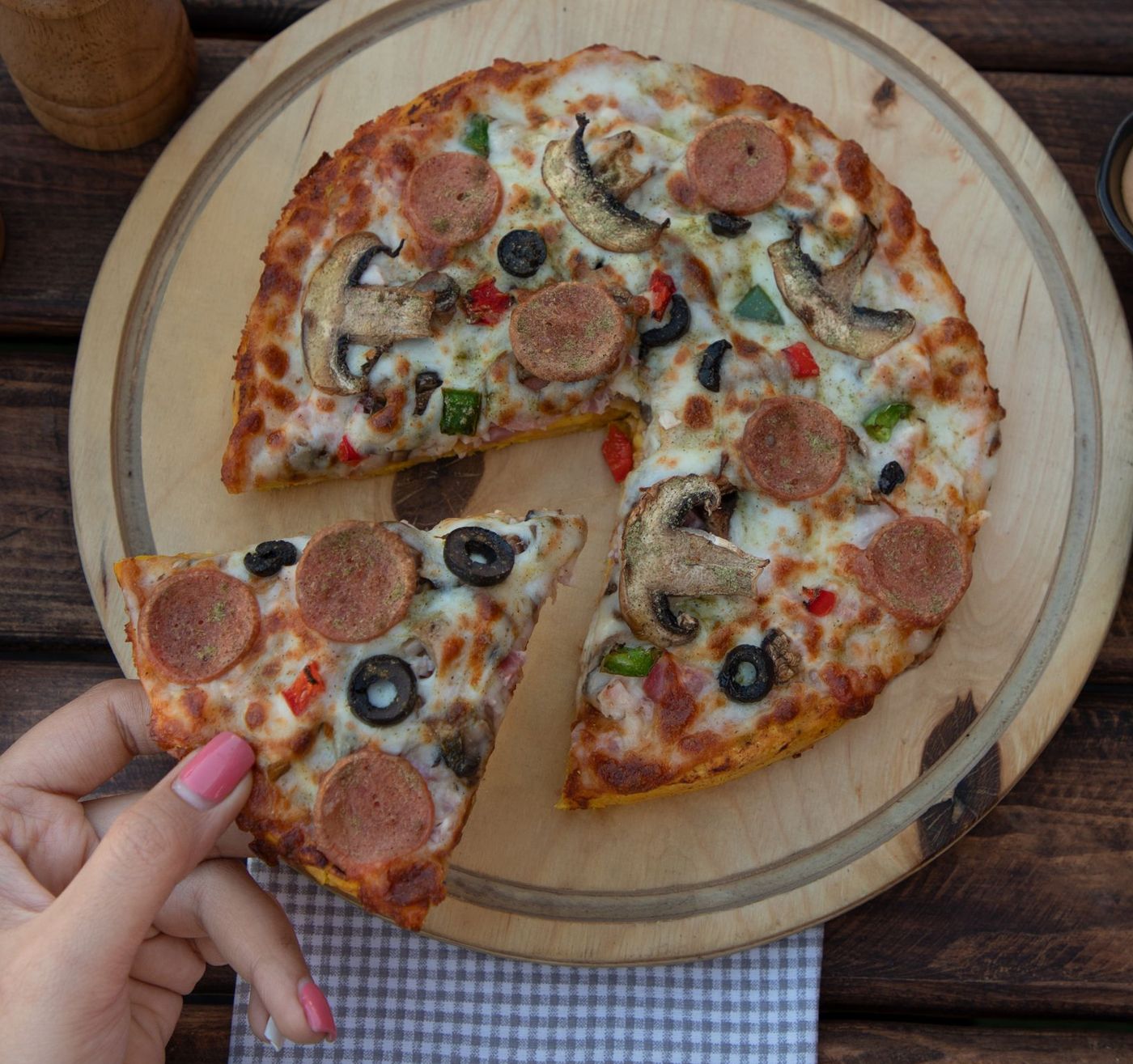 Loaded house special pizza with sausage rounds, mushrooms, black olives and peppers, one slice lifted by hand