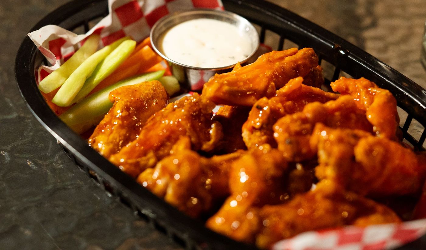 Basket of glossy buffalo chicken wings with celery and carrot sticks and a cup of ranch