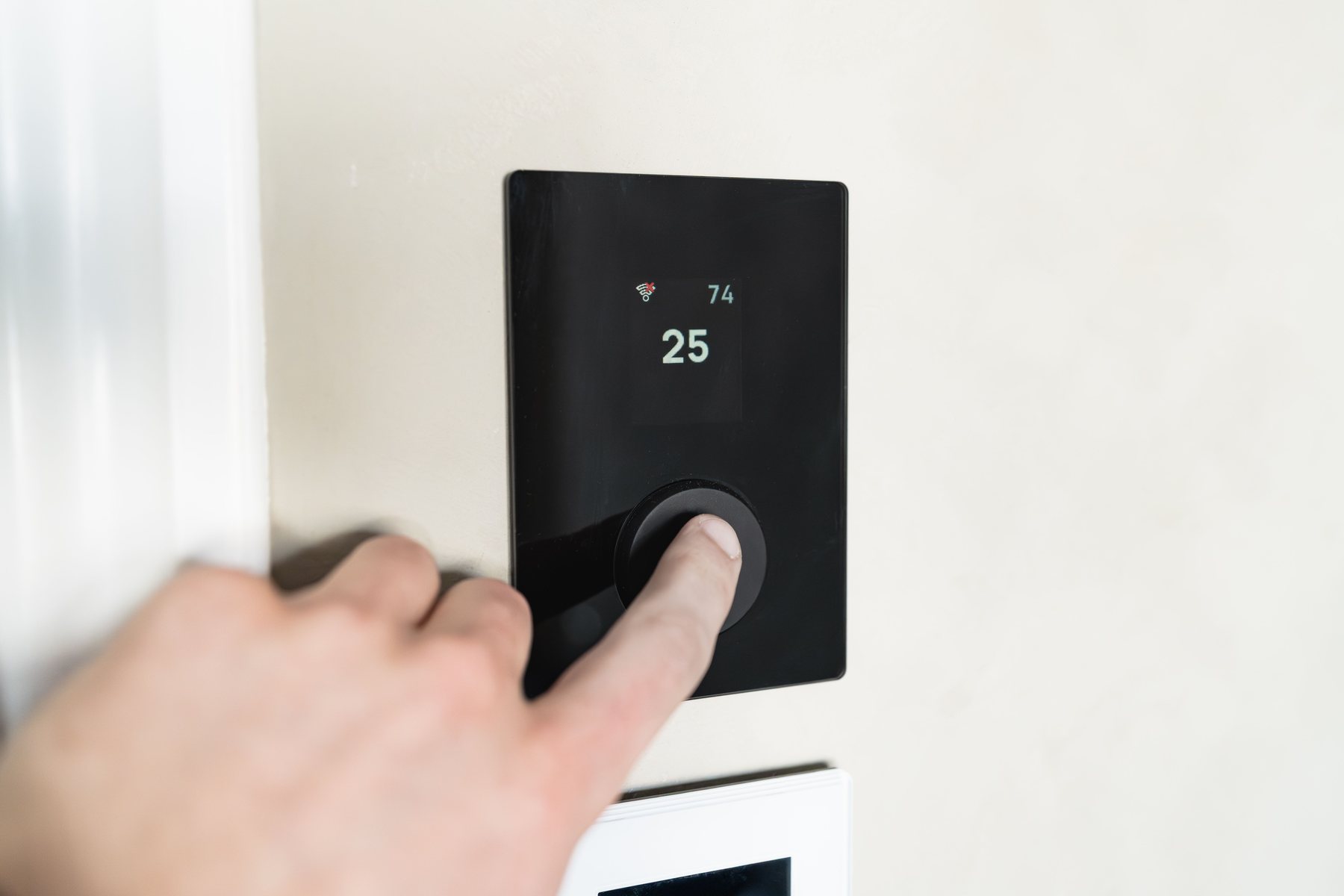 A hand adjusting the temperature on a wall thermostat