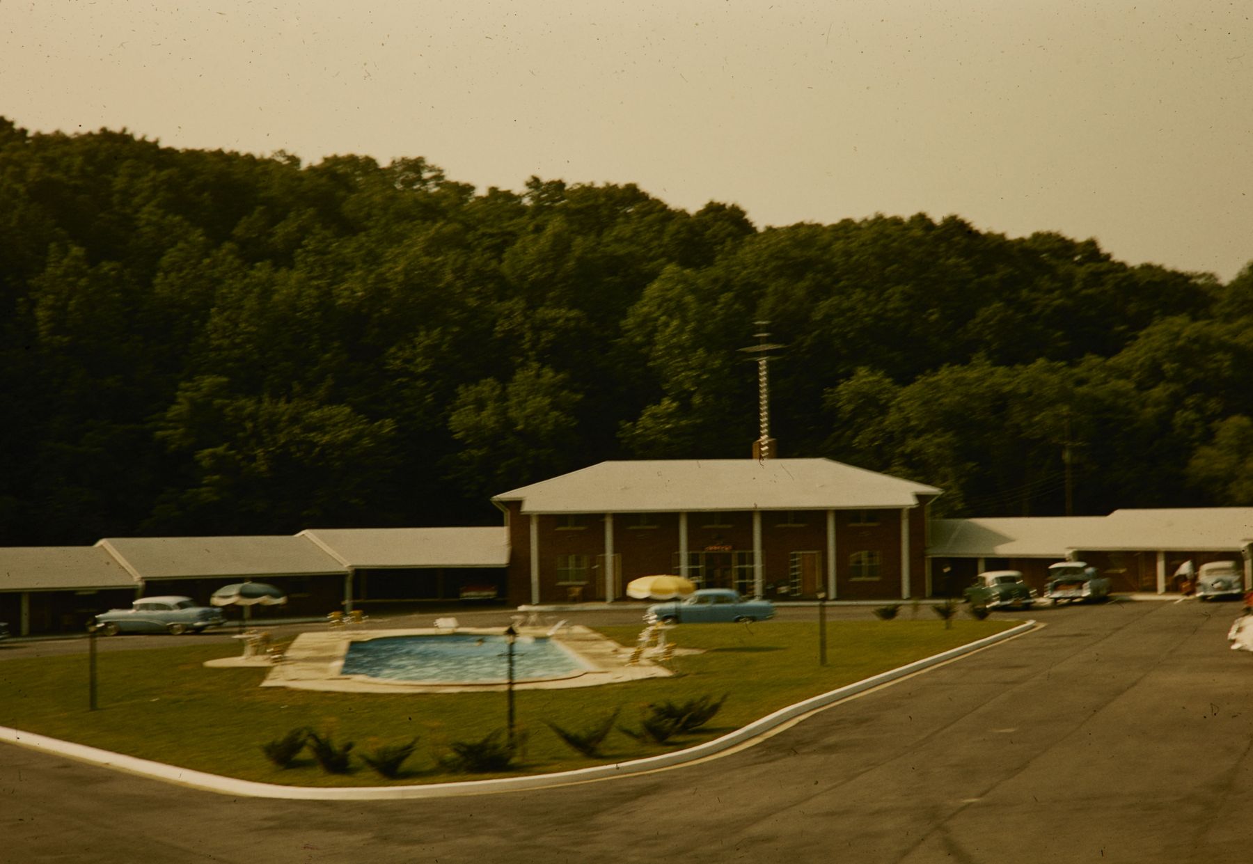 A pool set in front of a low building and trees